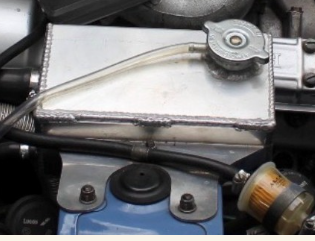 Triumph Stag alloy header tank installed on the engine bay, showing raised mounting position.