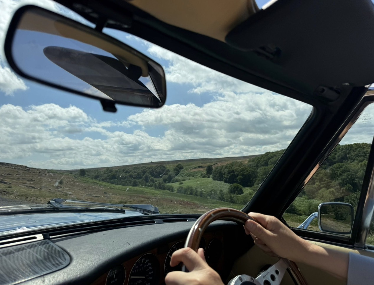 The wood-rimmed steering wheel and instrument binnacle of a Triumph Stag, with open moorland through the windscreen.