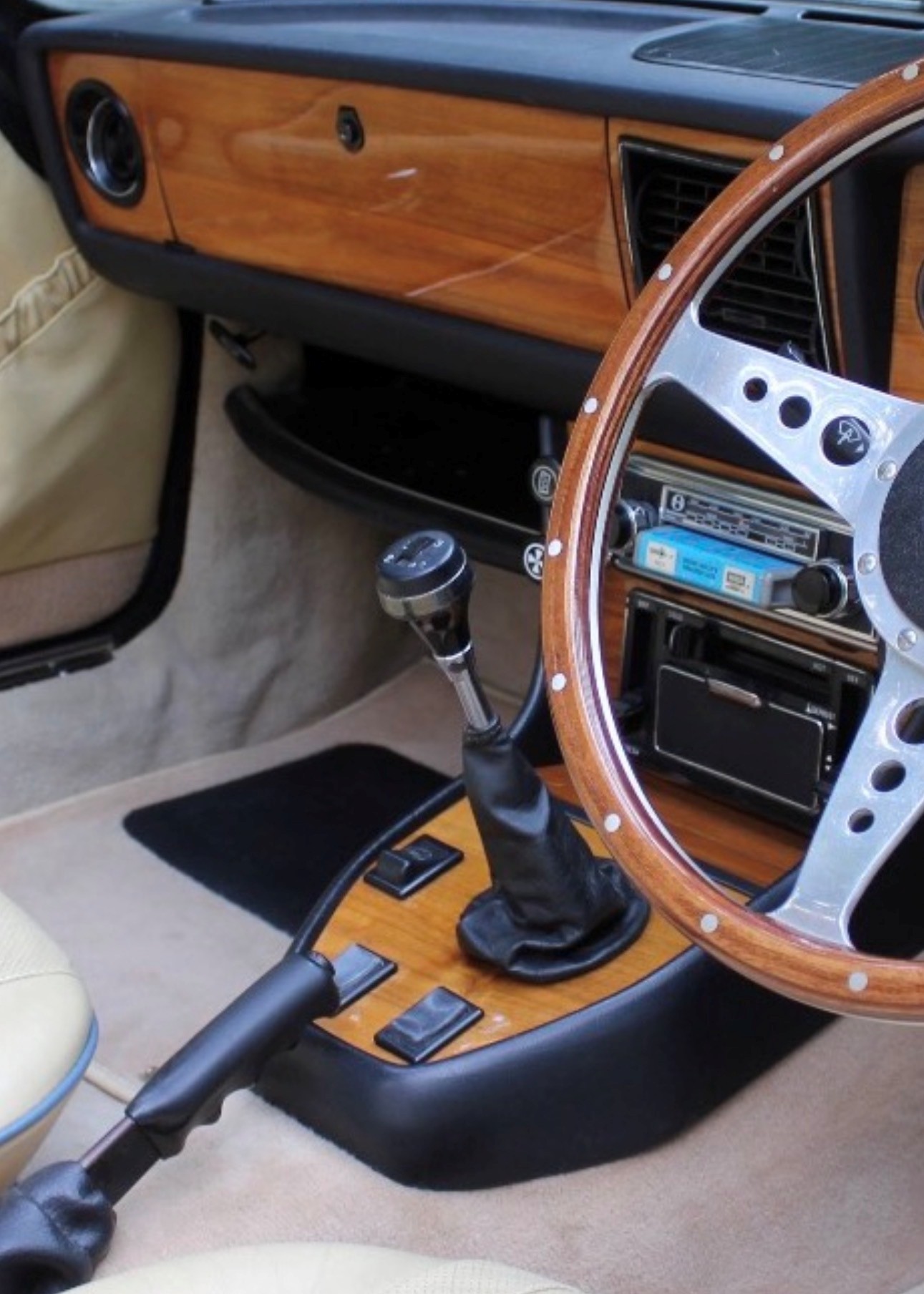 Triumph Stag manual gear lever and overdrive switch on the wood-veneer centre console, with wood-rim steering wheel and period radio.