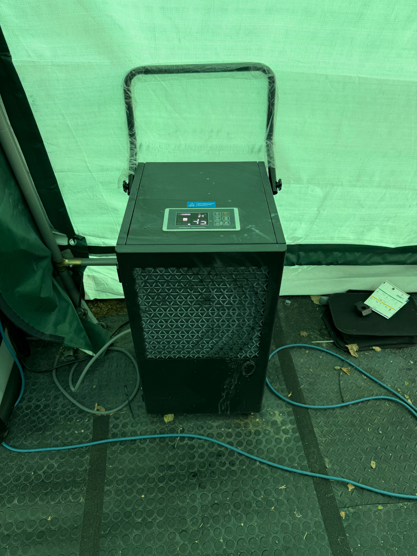 A dehumidifier running inside a temporary car shelter, showing the control panel and continuous drain hose setup.