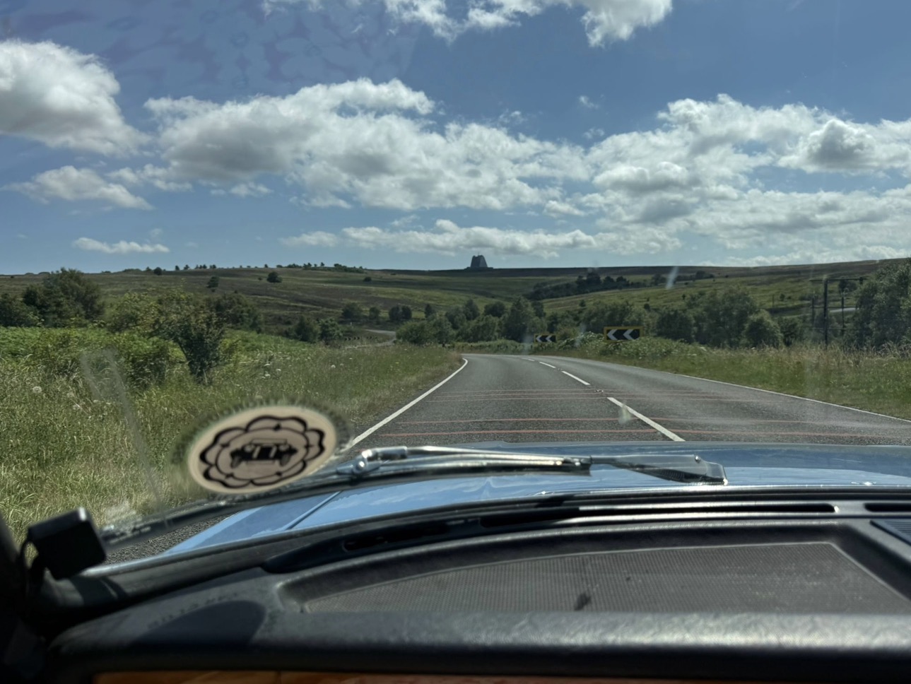 View forward down the A169 over the bonnet of a Triumph Stag, with chevron warning signs on a bend ahead and the RAF Fylingdales radar building on the horizon.